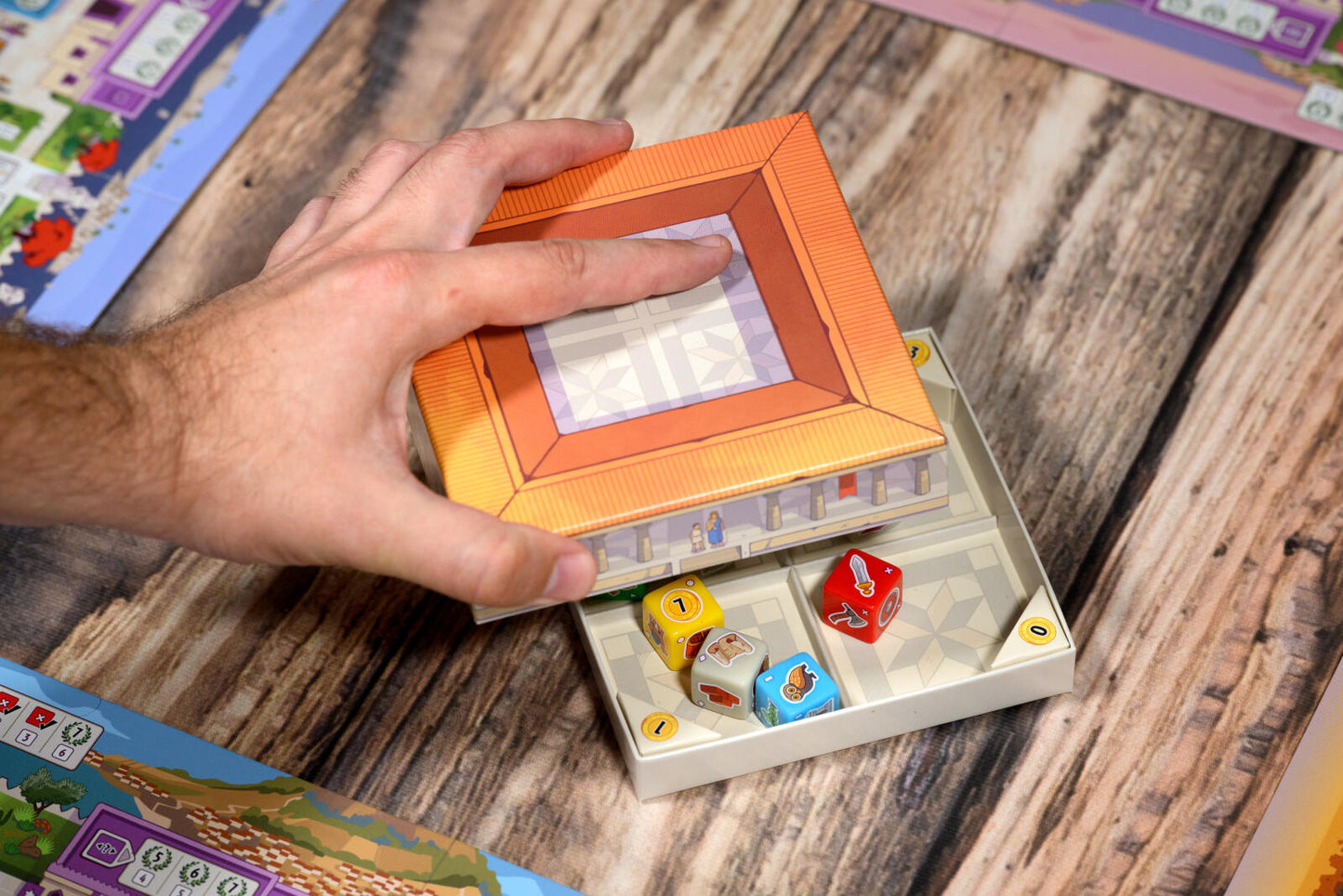 Hand opening a small box containing colorful dice on a wooden surface