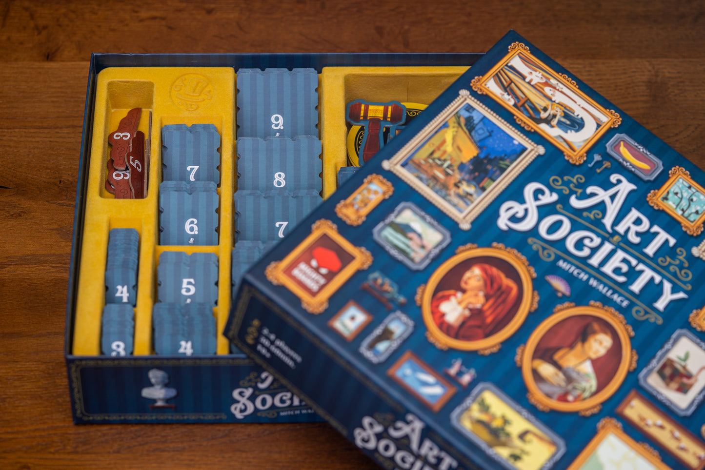 Board game box for 'Art Society' with cards and pieces on a wooden surface