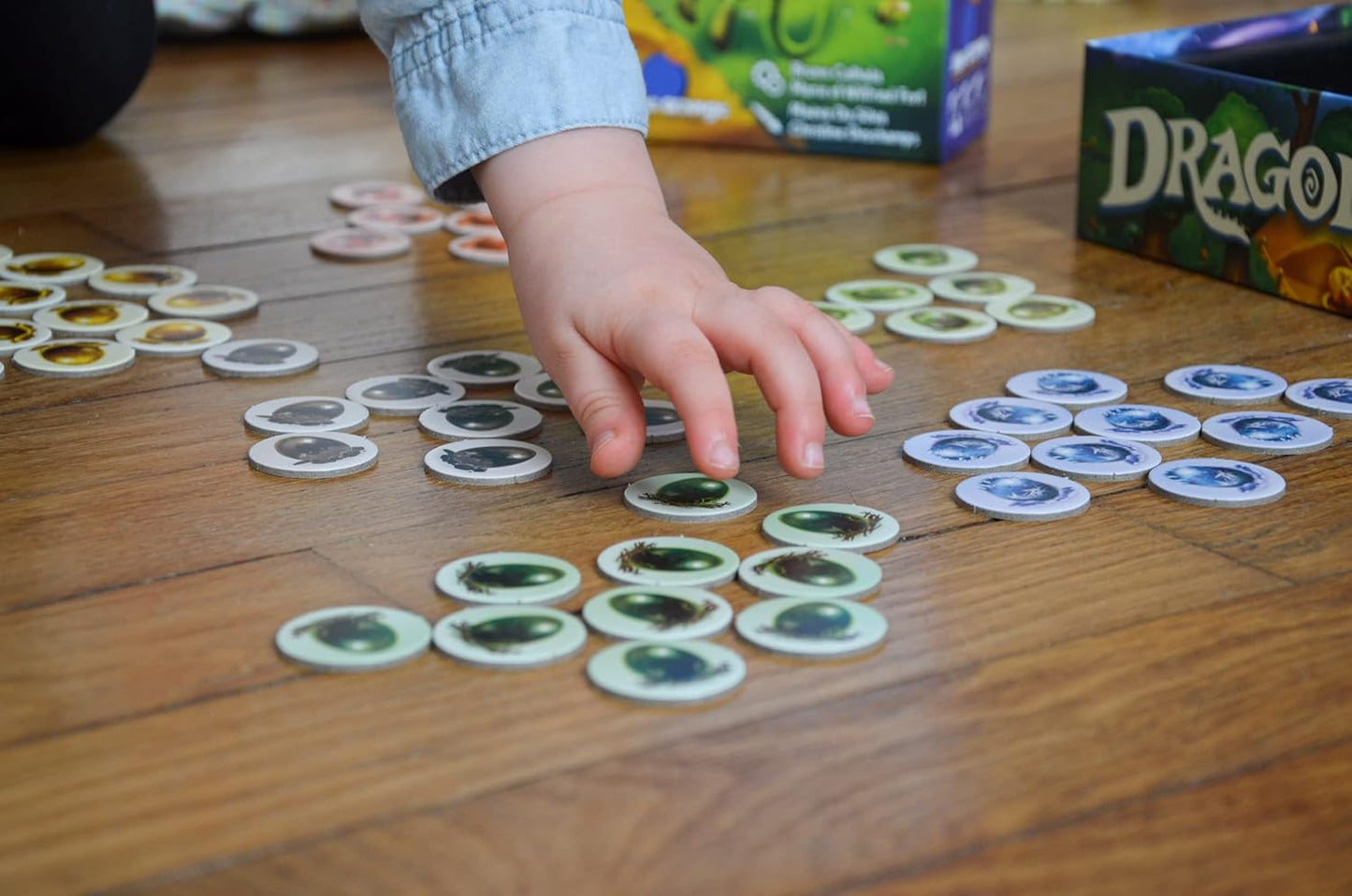 Child's hand reaching for game pieces on a wooden surface with a 'Dragon' box in the background.