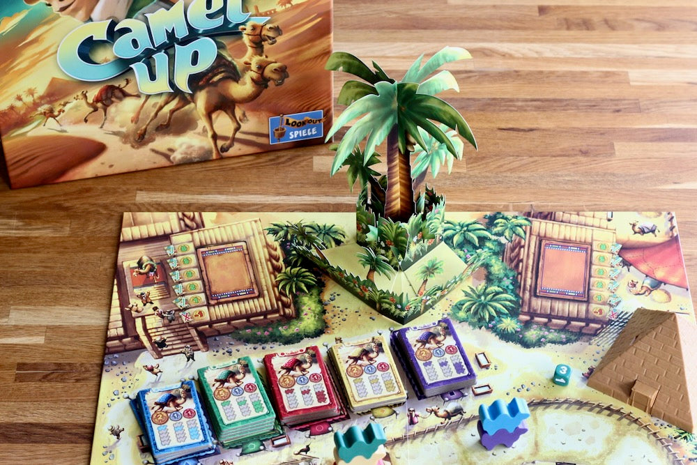 Board game setup with 'Camel Up' packaging and game pieces on a wooden surface