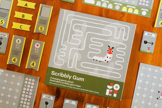 Scribbly Gum board game set displayed on a wooden tabletop, showing the central game board, cards, and game pieces arranged around it.