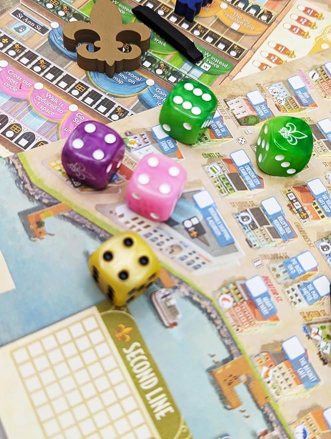 A close-up of a board game setup showing colorful game dice scattered across a detailed city-themed game board. The visible dice include purple, pink, green, yellow, and blue, with a wooden token piece near the top.