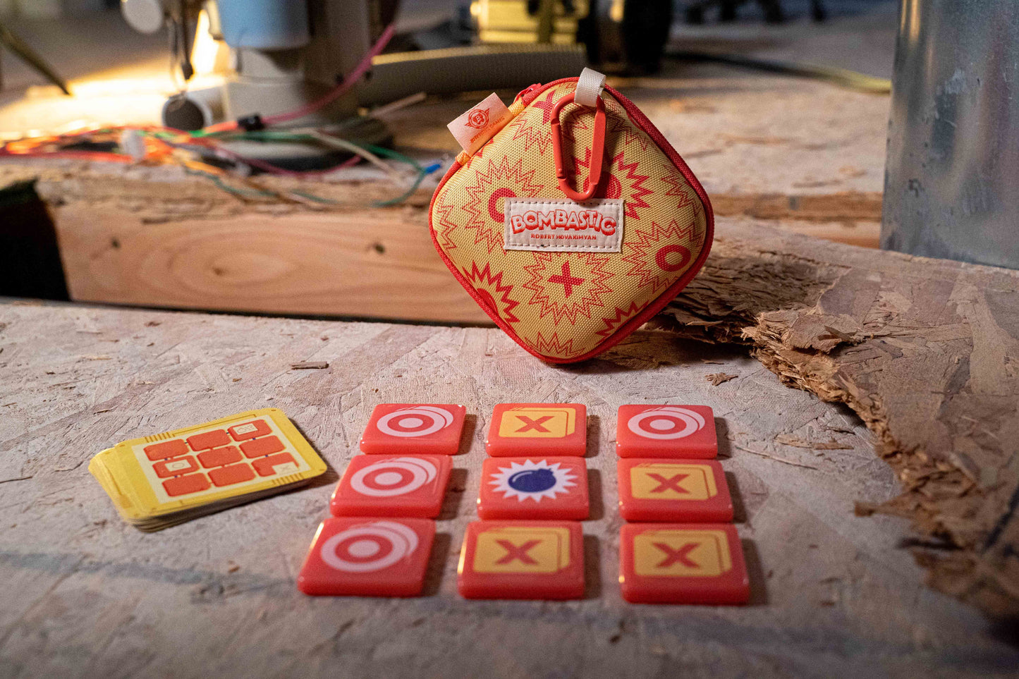 Bombastic Children's tic-tac-toe game set on a wooden surface with a red and yellow bag in the background.