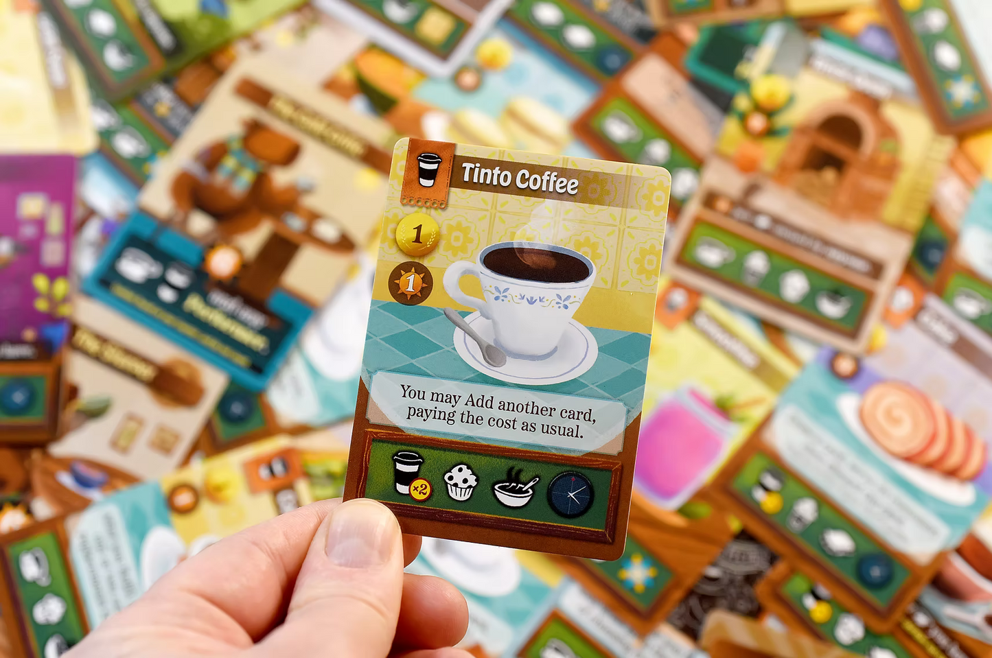 Cafe Baras Card from a board game held by a hand with colorful game pieces in the background