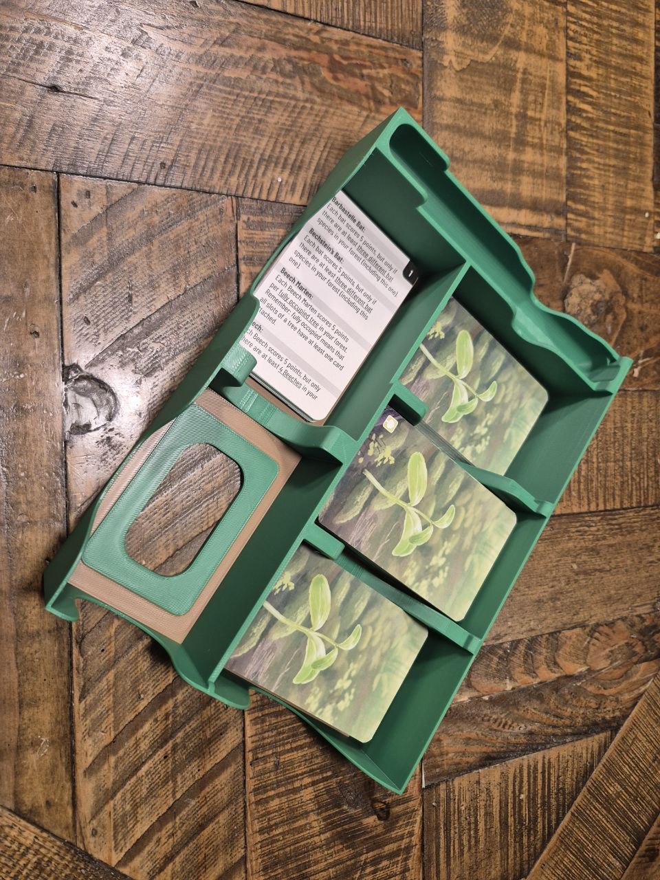 A green plastic card organizer tray containing gardening cards, photographed from above on a rustic wooden floor.