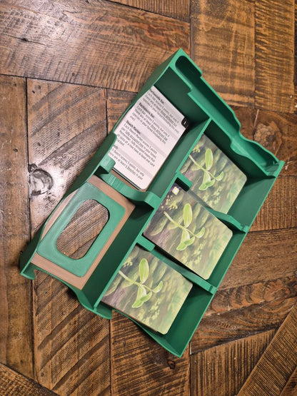A green plastic card organizer tray containing gardening cards, photographed from above on a rustic wooden floor.