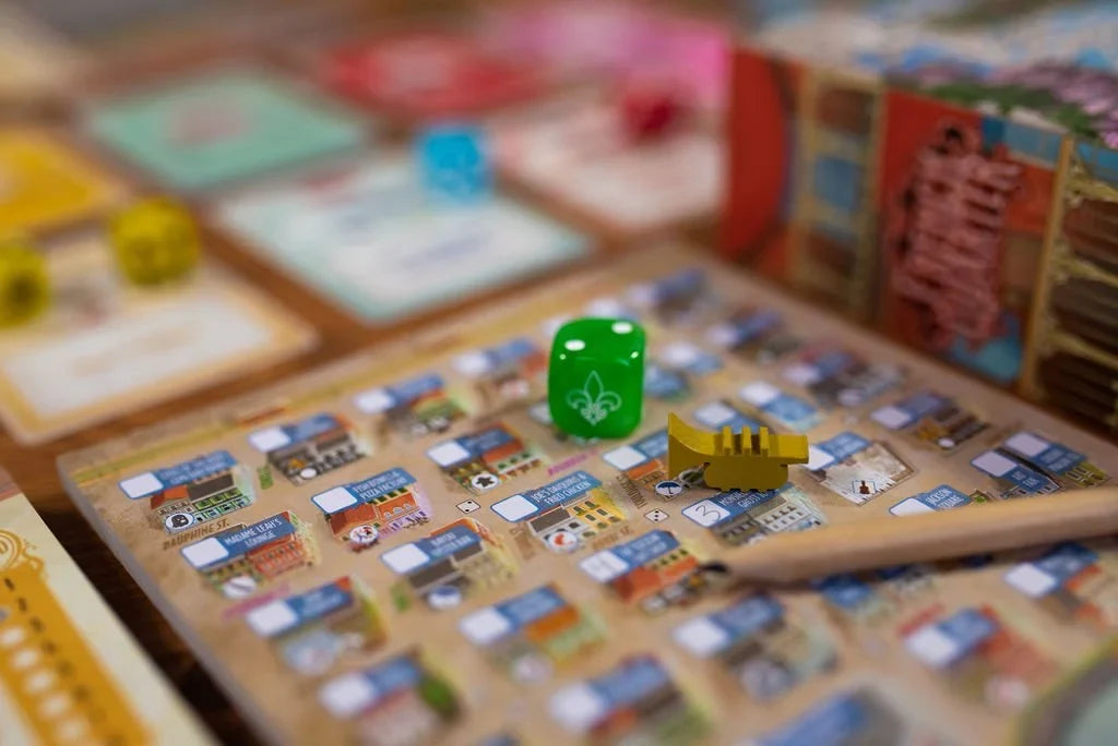A close-up of a board game board with a green translucent die and a yellow piece, with other game components blurred in the background.