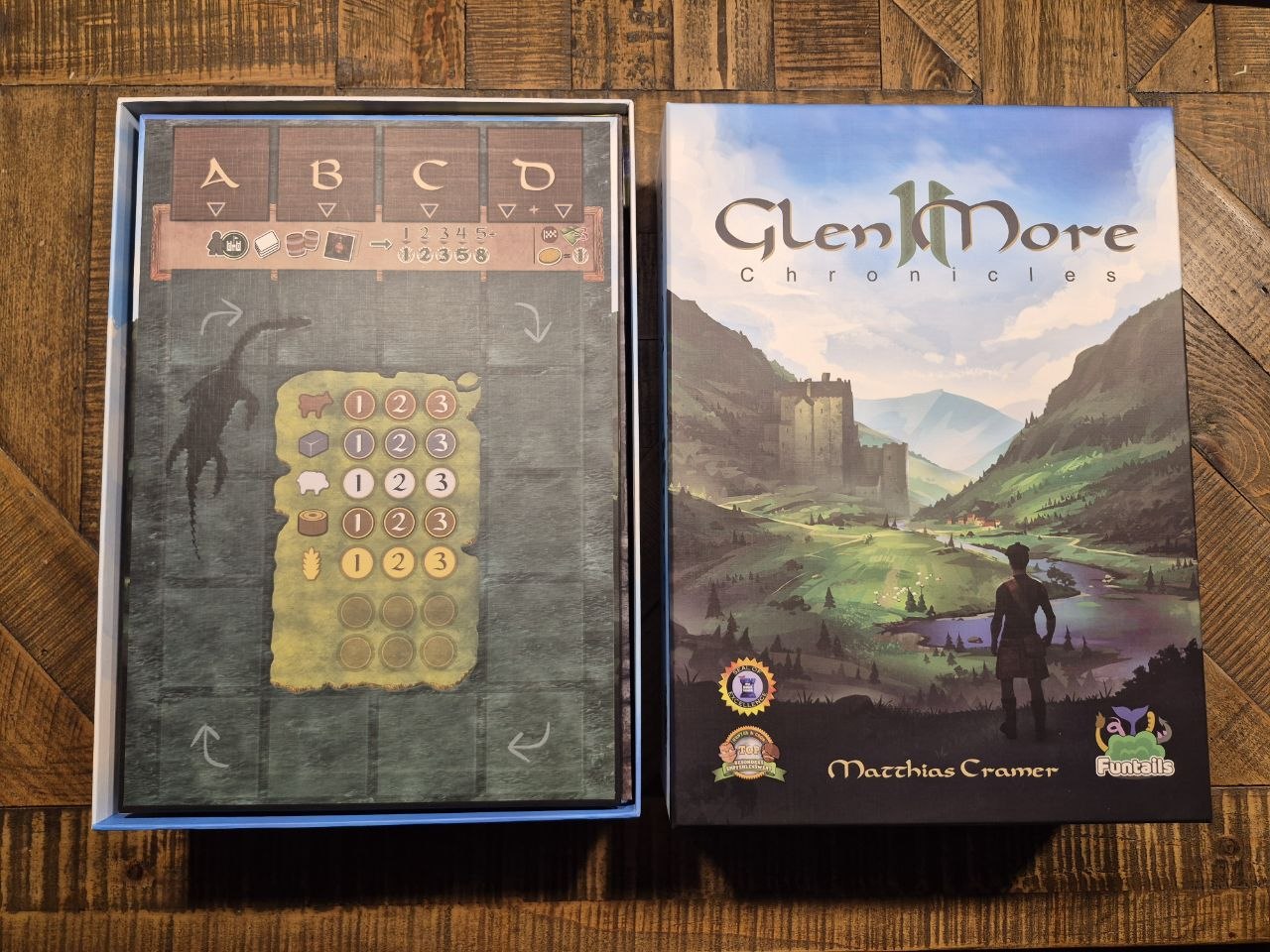 The board game box set for 'Glen More Chronicles' by Matthias Cramer, showing both the front cover art and the inner playmat packaging, placed on a wooden surface.