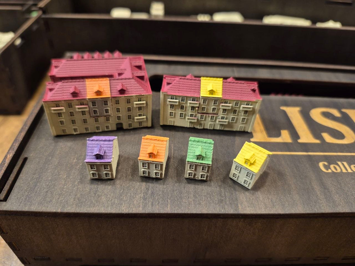 A set of miniature model houses and apartment buildings with various colored roofs, displayed on a dark wooden box from 3DLevelup's 'LISBOA Collection'.