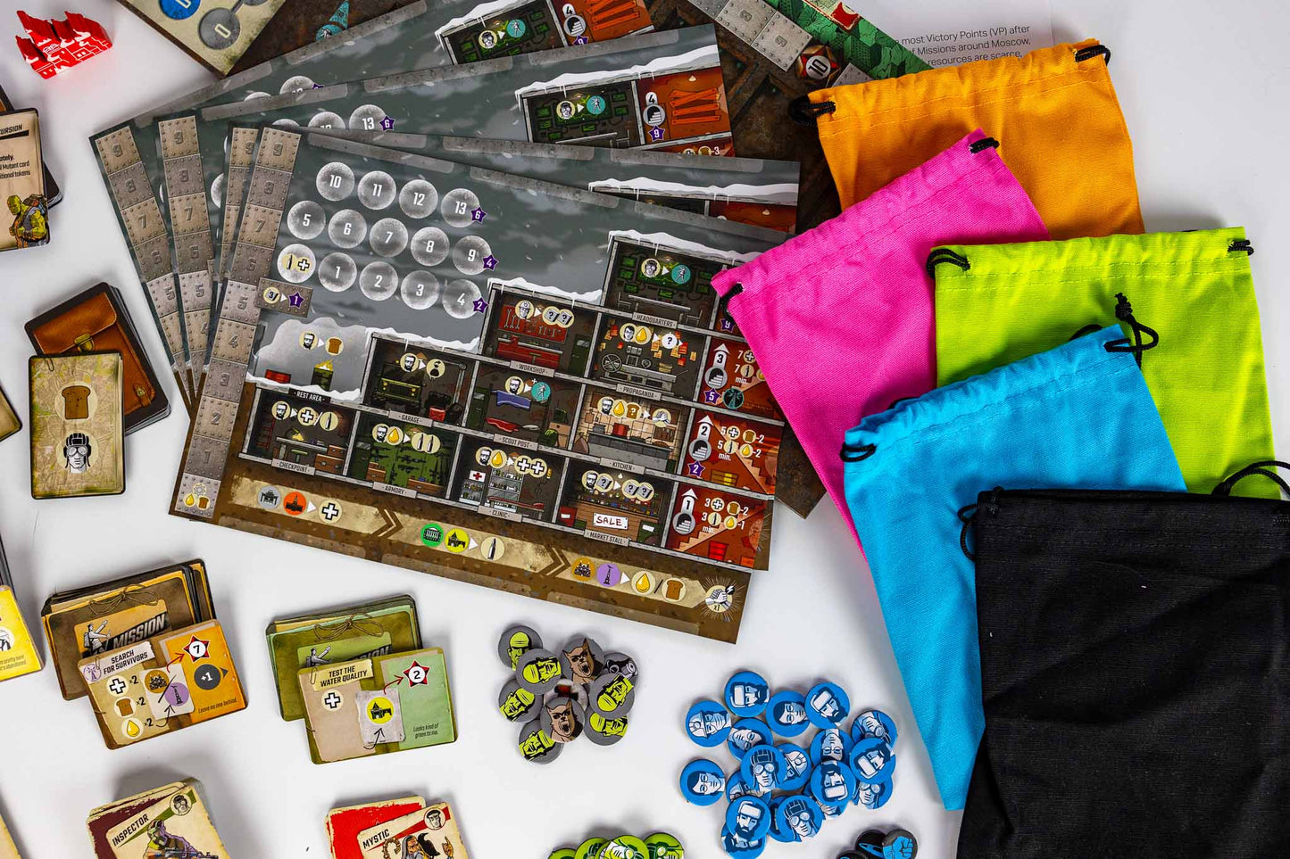 Resurgence Board game components and storage bags arranged on a white surface, including a game board, cards, tokens, and drawstring pouches in orange, pink, neon green, blue, and black.