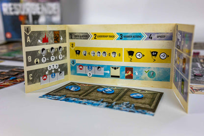 Resurgence board game setup showing an open playmat with colored action panels, cards, and tokens on a white tabletop.