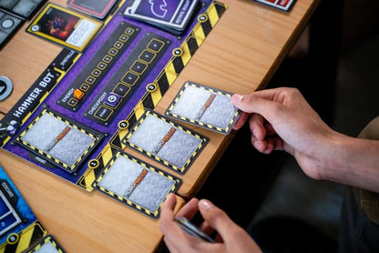 Person playing Robo Rally with a focus on cards and hands on a wooden table.