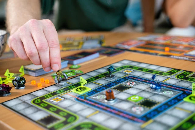 Board game Robo Rally in progress with players' hands and game pieces on a table.