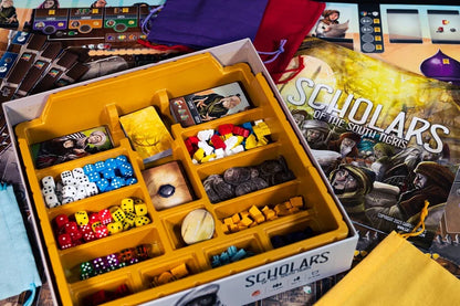 Scholars of the South Tigris Board game components including dice and pieces in a yellow box with 'Scholars' branding.