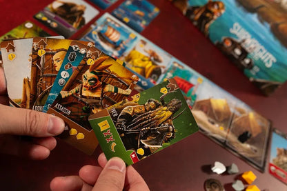 Shipwrights North Sea Close-up of hands holding board game cards with colorful illustrations on a red surface.