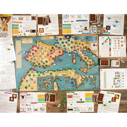 An overhead view of Tanto Monta board game set arranged on a wooden surface, featuring a large map board, multiple printed game sheets, cards, dice, and small brown boxes.