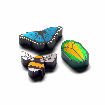 Three small insect-shaped accessories on a black background: a blue butterfly, a bumblebee, and a green beetle with yellow and orange wing patterns.