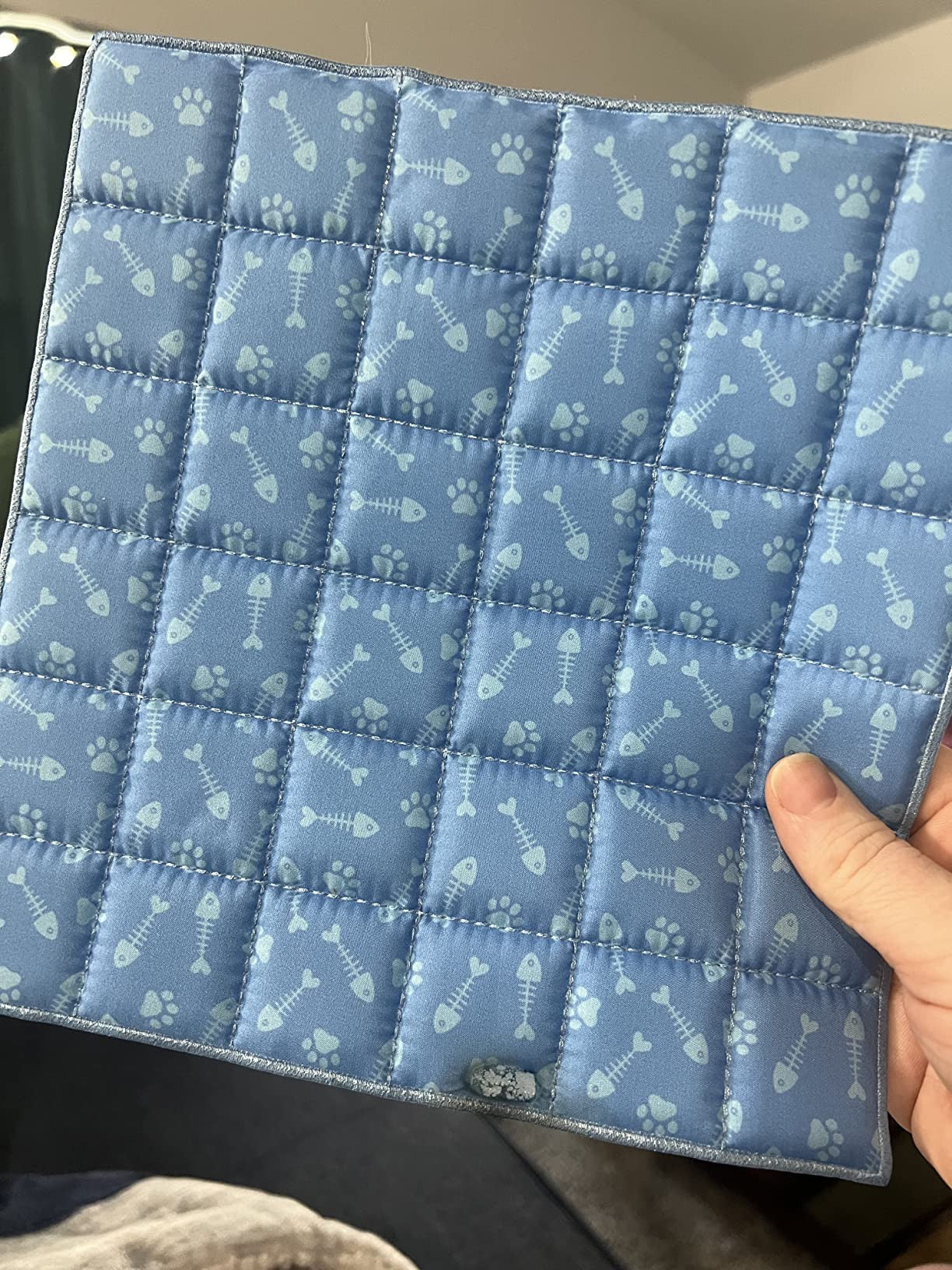 Boop Board game Blue quilted mat with paw and bone pattern held by a hand