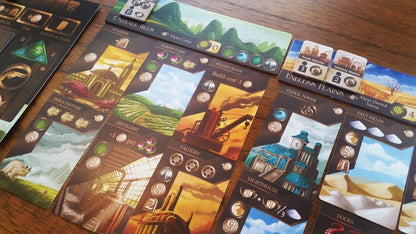 Board game components including cards and a board with scenic illustrations on a wooden surface.