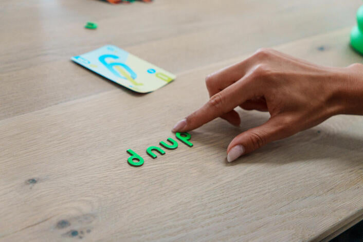 Hand arranging green letter tiles dnup  on a wooden surface