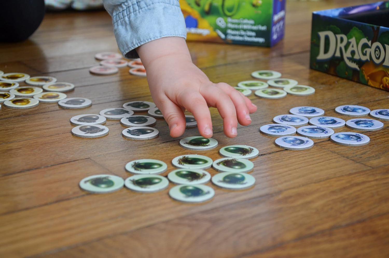 Child's hand reaching for game pieces on a wooden surface with a 'Dragon' box in the background.