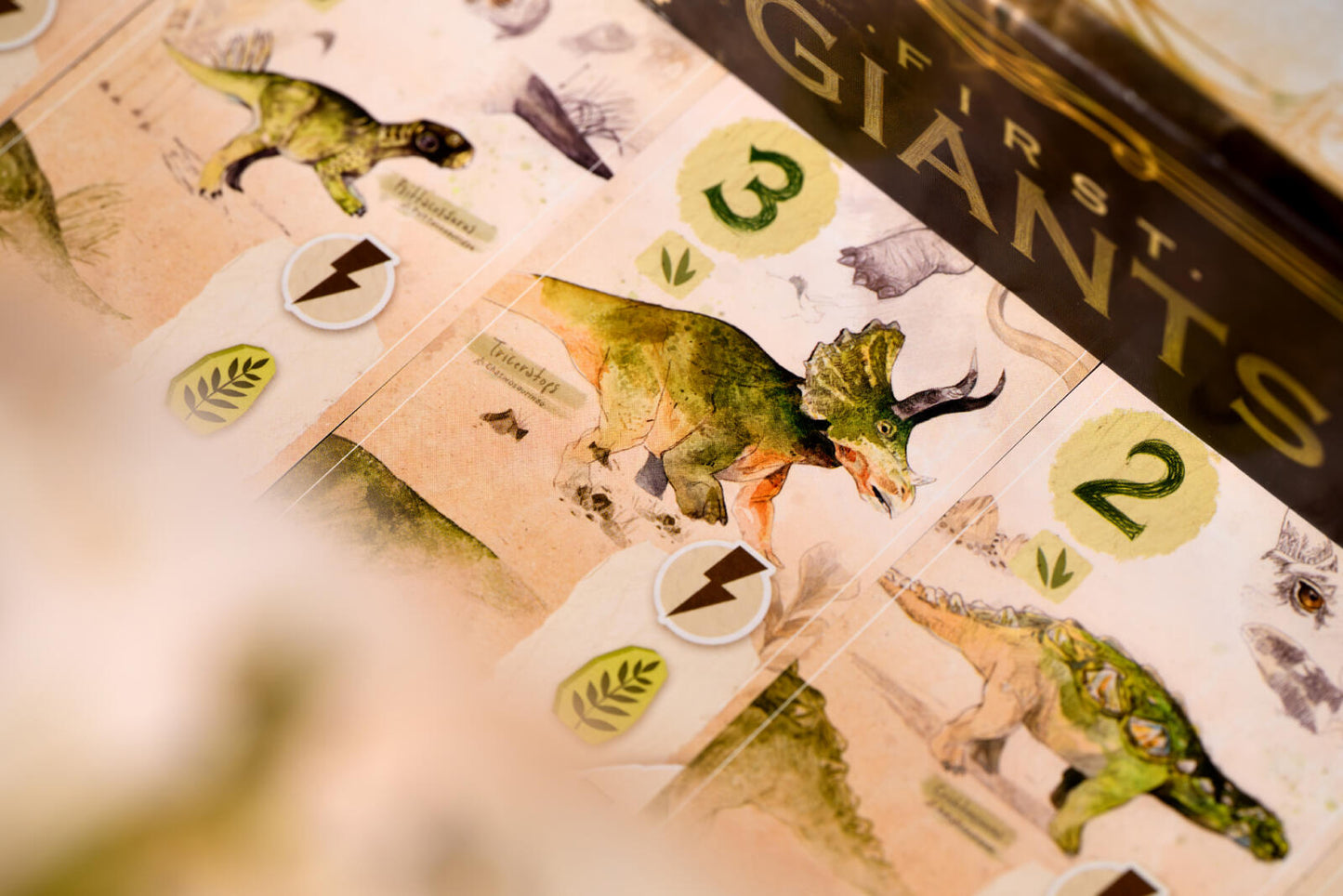 Close-up of 'First Giants' board game pieces with dinosaur illustrations and numbers.