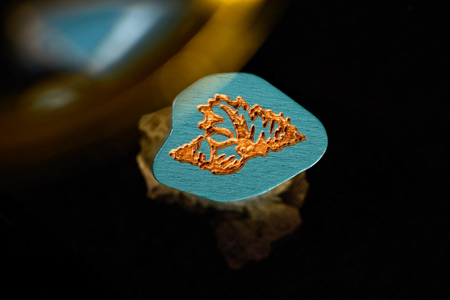 Wooden guitar pick with leaf design on a dark background