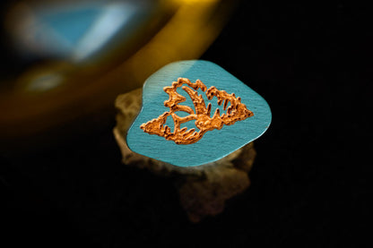 Wooden guitar pick with leaf design on a dark background