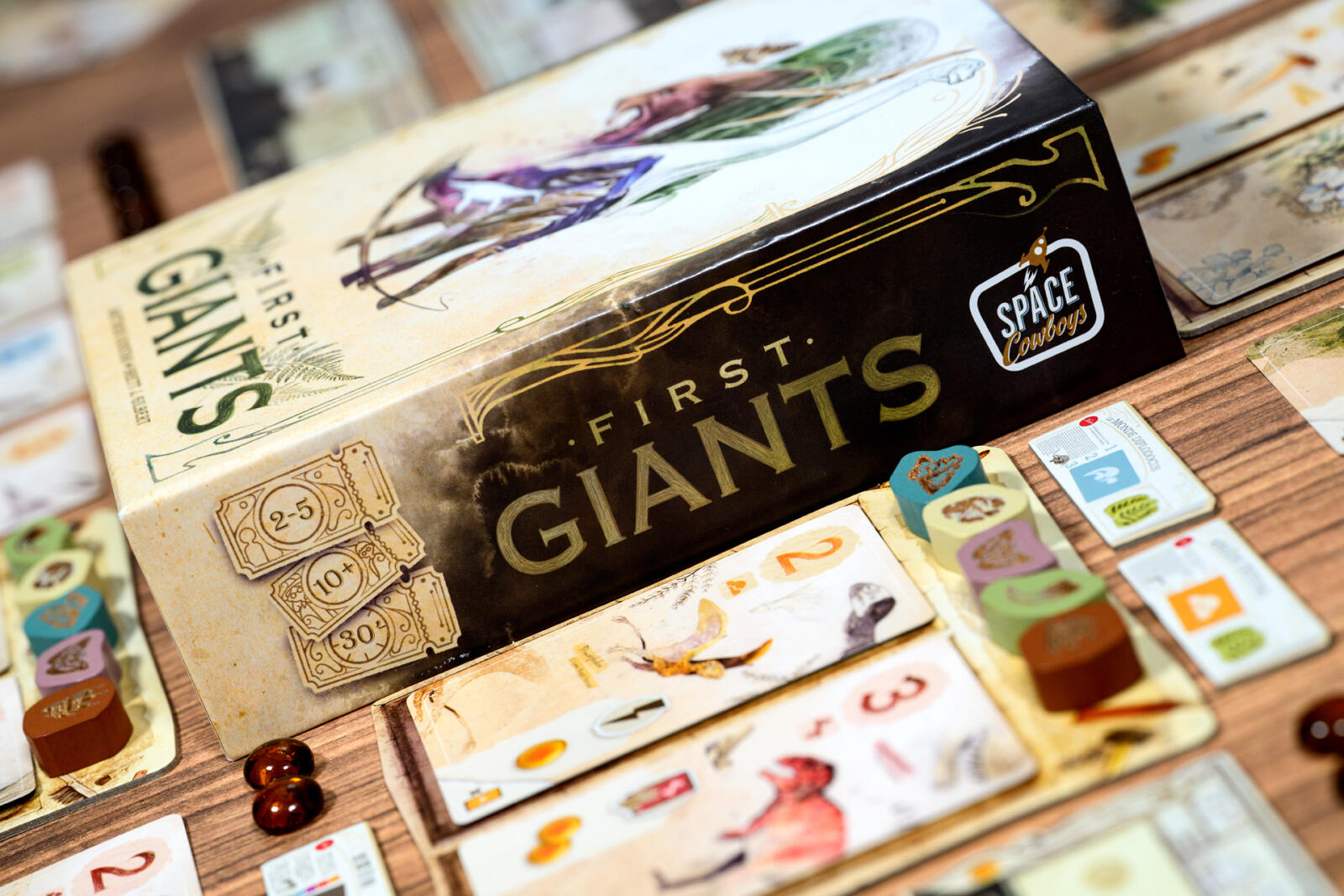Board game box for 'First Giants' by Space Cowboys on a wooden table with game pieces.