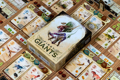 Board game box titled 'Of First Giants' surrounded by game cards on a wooden surface