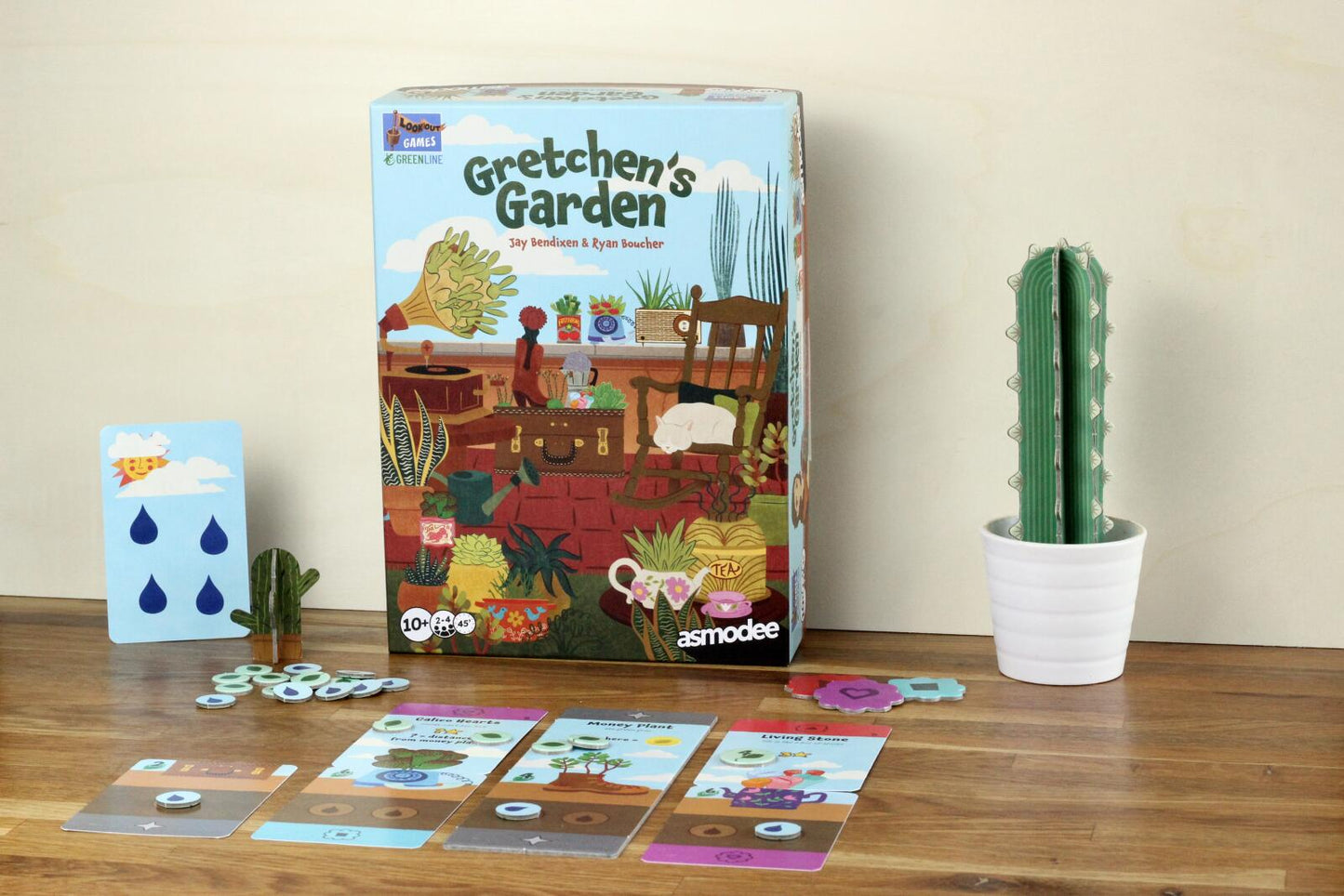 Board game box titled 'Gretchen's Garden' on a wooden surface with cards and a cactus.