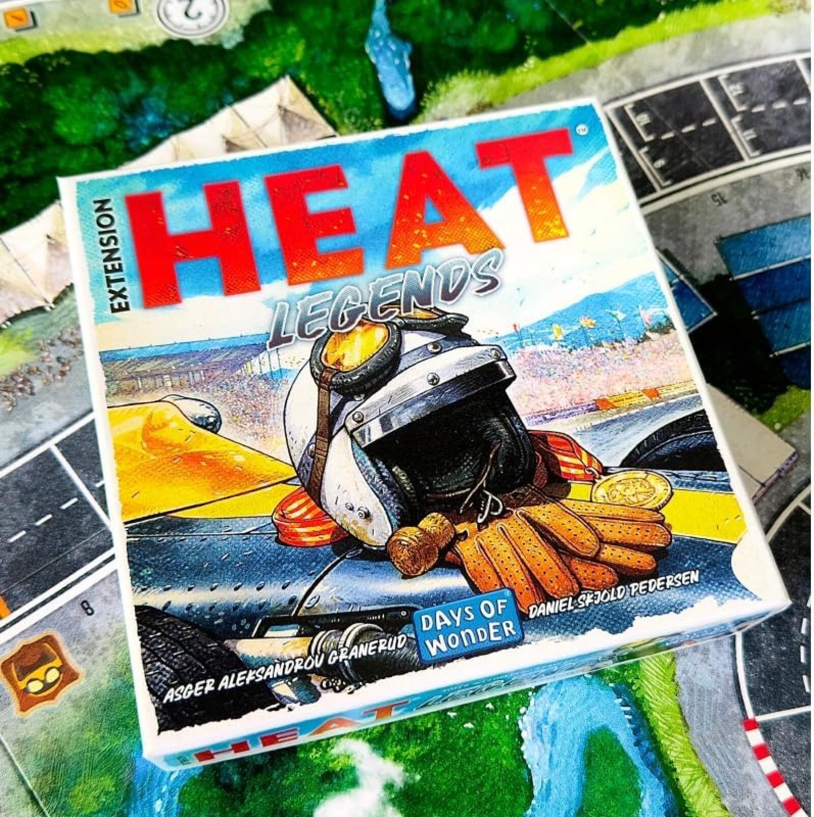 The board game box for 'Heat Legends: Days of Wonder' expansion is shown at an angle, resting on a green and blue illustrated game board. The box features a colorful illustration of a race car driver in a helmet with a yellow sun visor, and the title 'HEAT LEGENDS' in large red and white letters.
