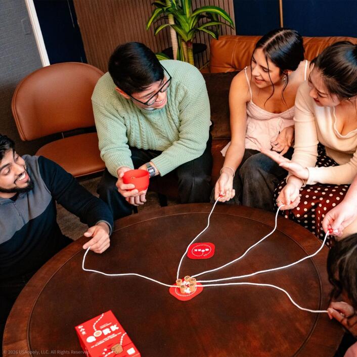 Group of people playing a game with red cups and strings on a wooden table.