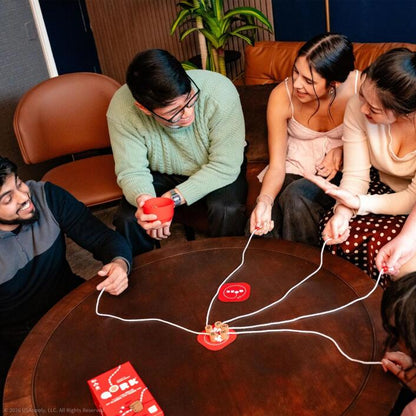 Group of people playing a game with red cups and strings on a wooden table.