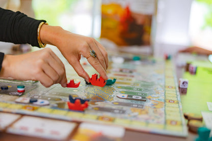 Person playing the River of Gold board game with colorful pieces on a table.