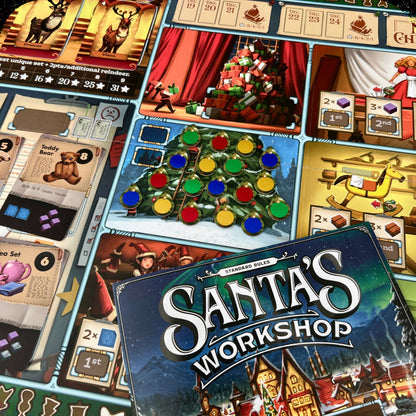 Close-up of the board game box for Santa's Workshop, surrounded by illustrated game boards and holiday-themed cards on a tabletop.