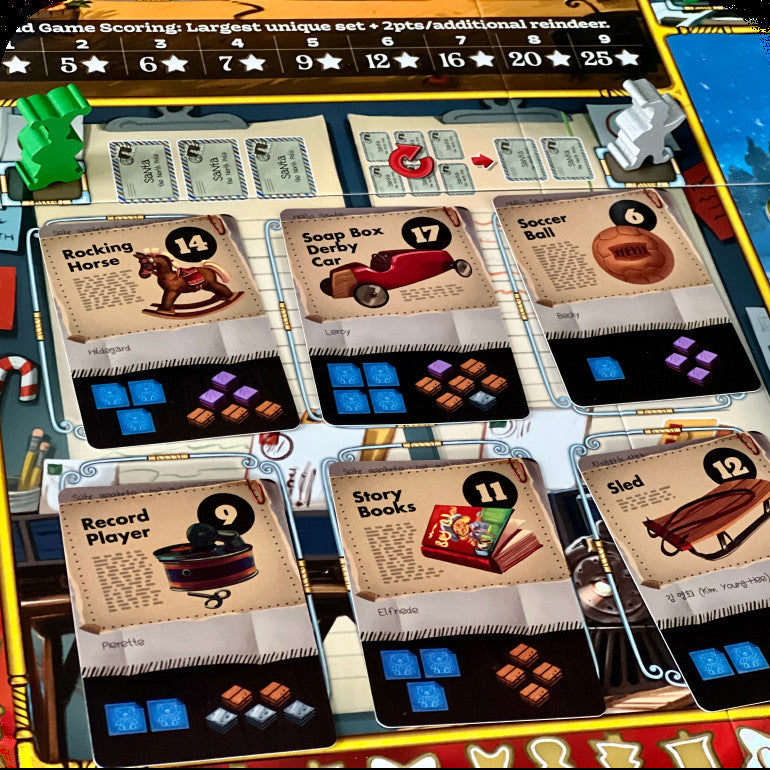 A close-up of a board game setup showing several toy-themed cards laid out on a game board, including Rocking Horse, Soap Box Derby Car, Soccer Ball, Record Player, Story Books, and Sled. The board has colorful sections, tokens, and other game pieces visible around it.