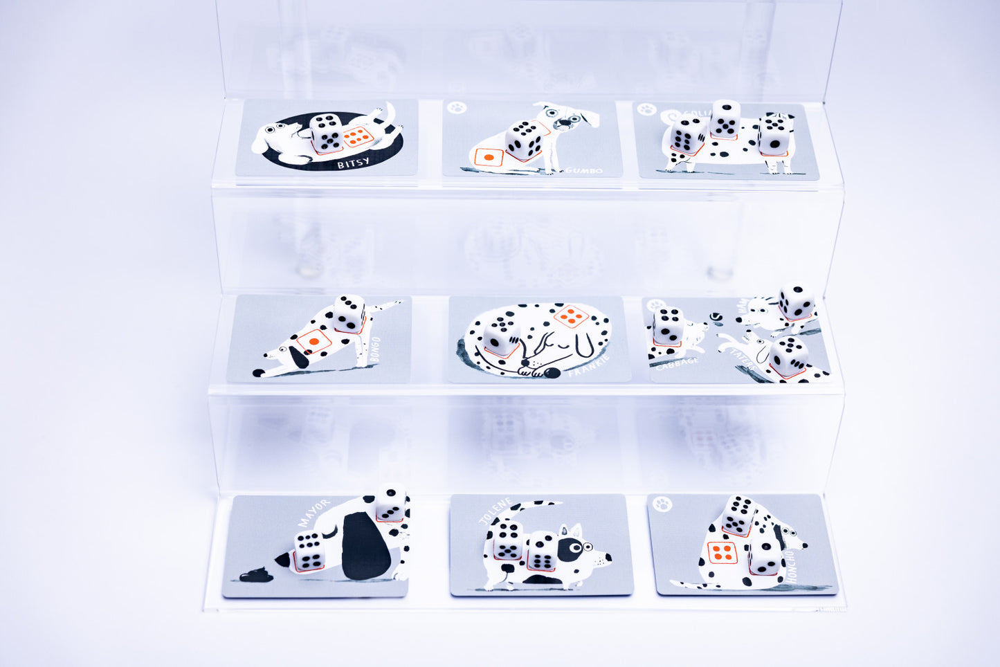 Nine rectangular cards or tiles displayed on clear acrylic shelves against a white background. Each tile features a black-and-white dalmatian-like dog illustration with black playing cards and dice motifs, plus small orange and red accents.