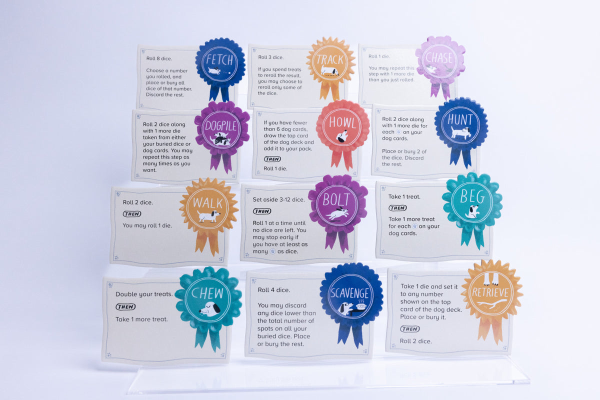 A set of dog training cards arranged in a pyramid on clear acrylic stands. Each card features a colorful circular badge with a different dog-related color, such as blue, purple, orange, and teal, with white text on the cards.