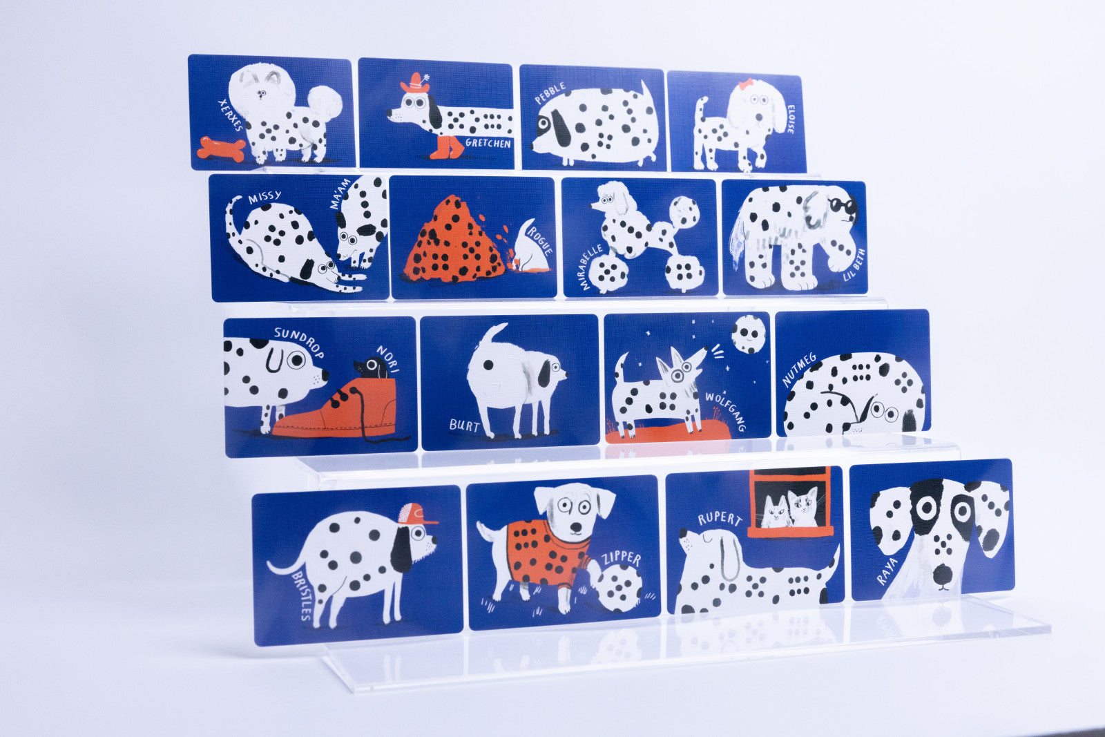 A set of rectangular blue cards featuring whimsical Dalmatian-themed illustrations and text, arranged in a staggered stack on a clear acrylic display stand against a white background.