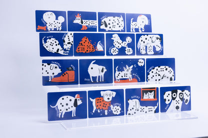 A set of rectangular blue cards featuring whimsical Dalmatian-themed illustrations and text, arranged in a staggered stack on a clear acrylic display stand against a white background.