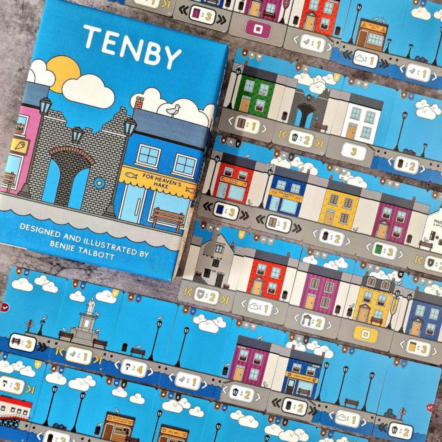 Board game titled 'Tenby' with colorful illustrations of a town on a blue background.