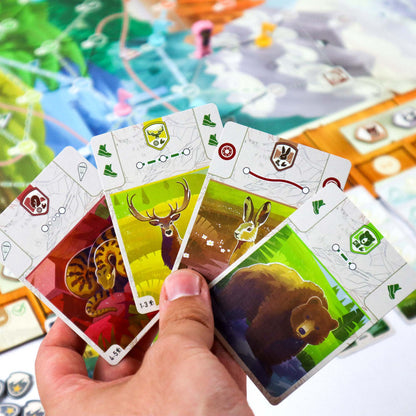 The Peak Team Hand holding animal-themed cards with a board game in the background