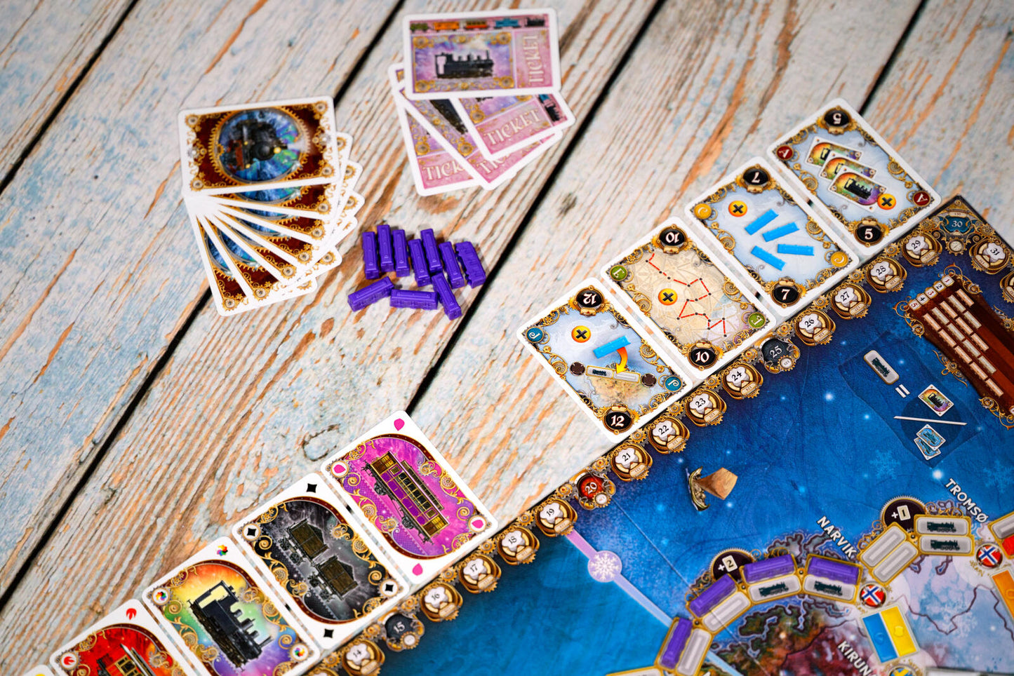 Ticket to ride northern lights Board game components arranged on a rustic wooden surface, including a blue game board, cards, gold-colored tokens, and purple pieces.