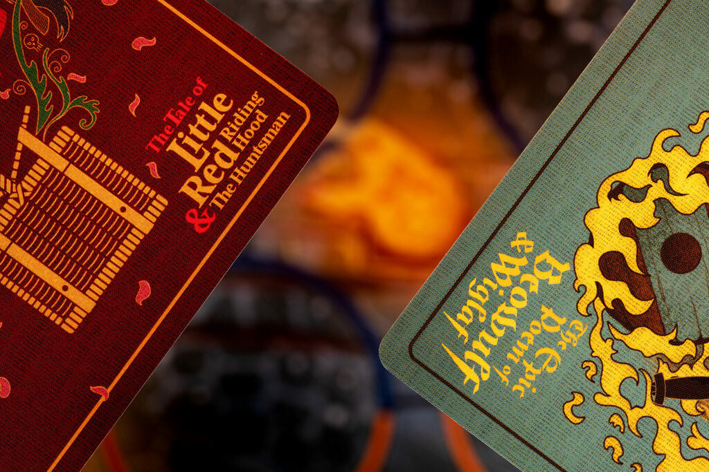 Two illustrated book covers or cards shown diagonally in a close-up. The left cover is dark red with gold and orange text reading 'The Fate of Little Red & the Huntsman.